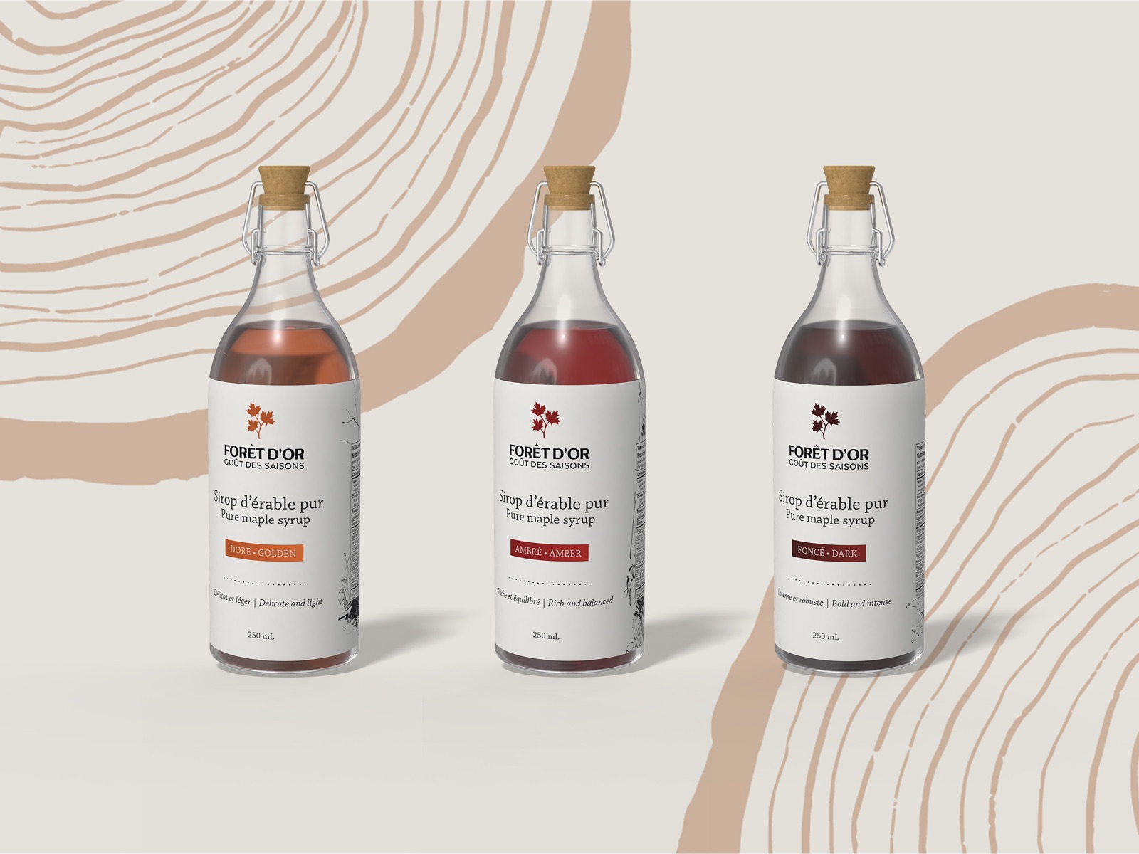 Three Forêt d'Or maple syrup bottles, golden, amber and dark, on a tree-ring pattern